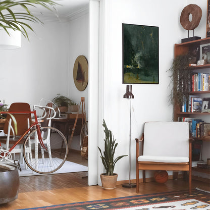 Eclectic living room with a road bike, bookshelf and house plants that features framed artwork of a Black and Gold above a chair and lamp