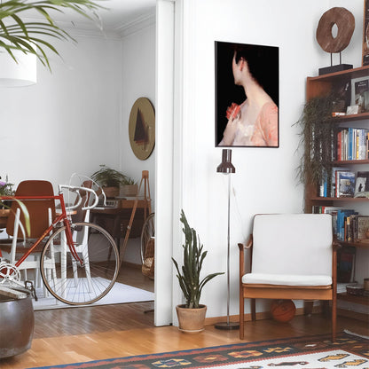 Eclectic living room with a road bike, bookshelf and house plants that features framed artwork of a Gilded Age Woman in Pink above a chair and lamp