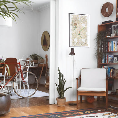 Eclectic living room with a road bike, bookshelf and house plants that features framed artwork of a Unfinsihed Flower above a chair and lamp