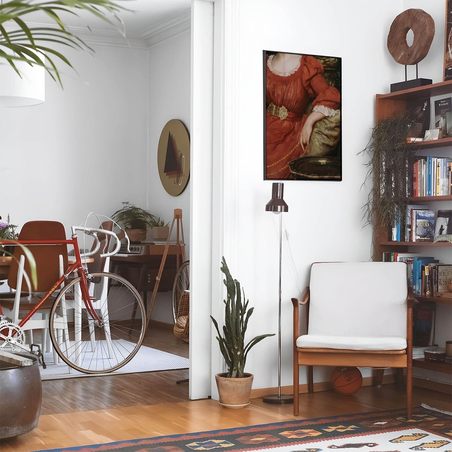 Eclectic living room with a road bike, bookshelf and house plants that features framed artwork of a Woman Posing in the Red Dress above a chair and lamp