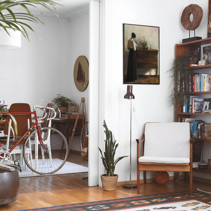 Eclectic living room with a road bike, bookshelf and house plants that features framed artwork of a Woman Reading by a Dark Cabinet above a chair and lamp