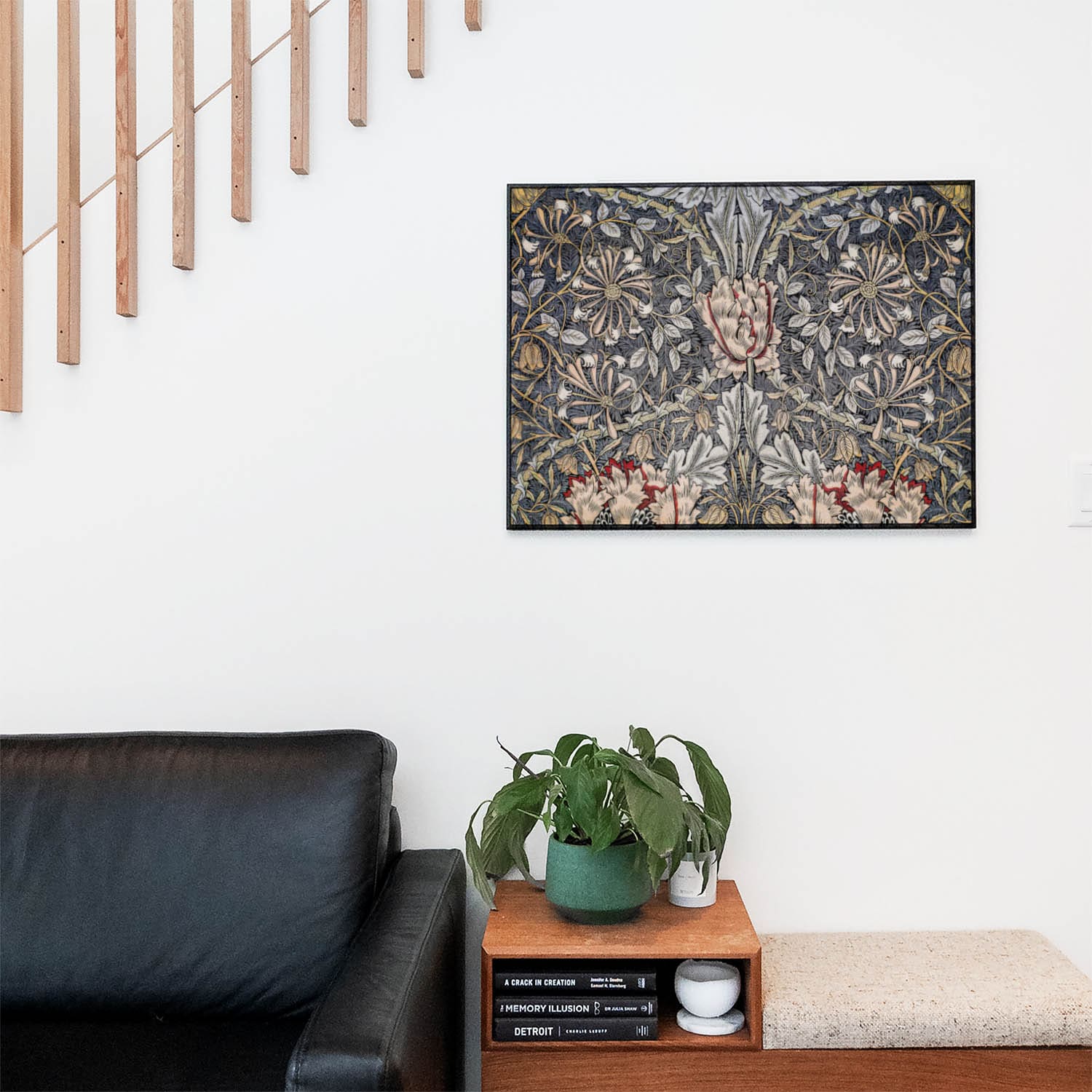 Living space with a black leather couch and table with a plant and books below a staircase featuring a framed picture of Plants and Flowers