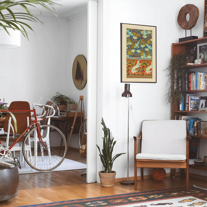 Eclectic living room with a road bike, bookshelf and house plants that features framed artwork of a Horses and Hummingbirds above a chair and lamp