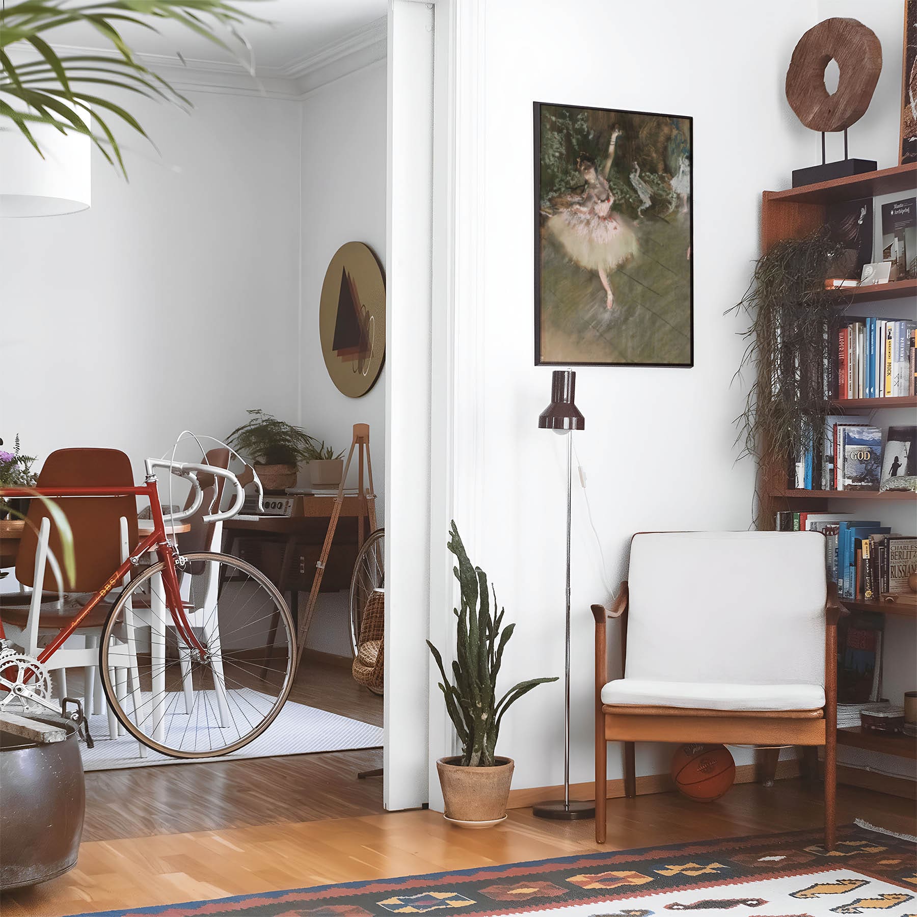Eclectic living room with a road bike, bookshelf and house plants that features framed artwork of a Ballet Dancer above a chair and lamp