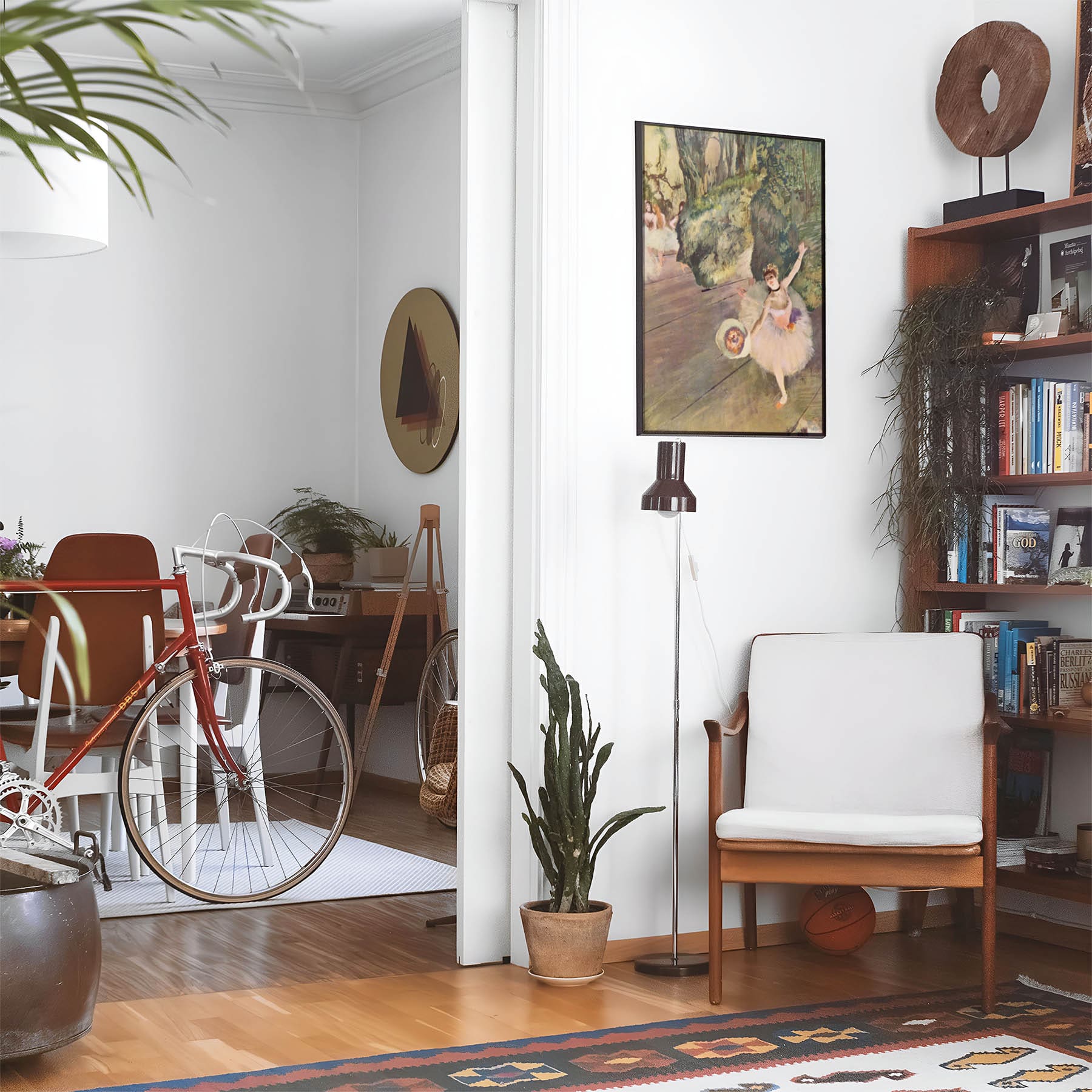 Eclectic living room with a road bike, bookshelf and house plants that features framed artwork of a Light Pink and Sage Green Dancer above a chair and lamp