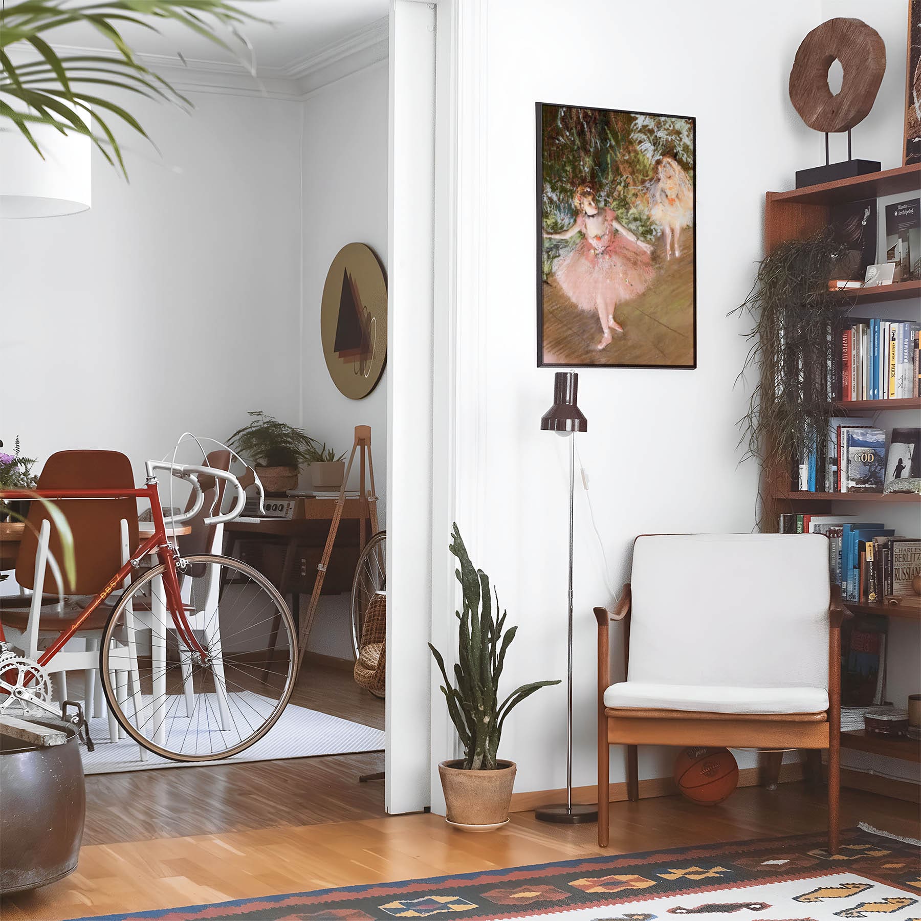 Eclectic living room with a road bike, bookshelf and house plants that features framed artwork of a Impressionist Ballet above a chair and lamp