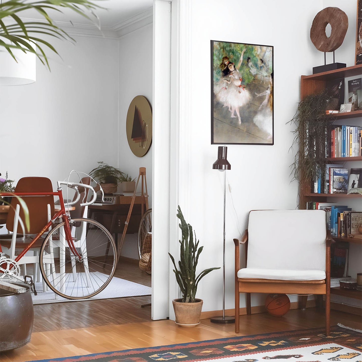 Eclectic living room with a road bike, bookshelf and house plants that features framed artwork of a White Dressed Ballerina above a chair and lamp