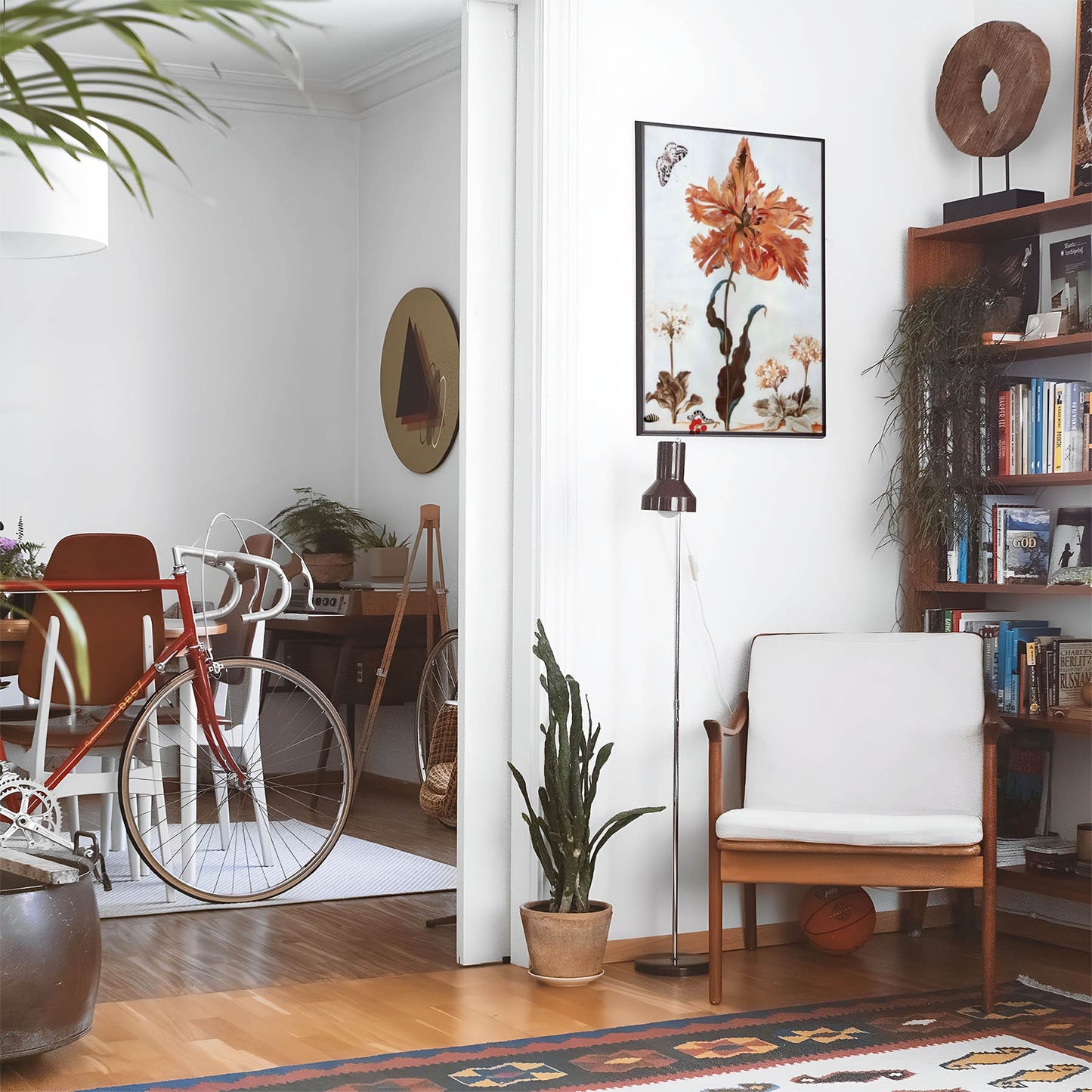 Eclectic living room with a road bike, bookshelf and house plants that features framed artwork of a Botanical Nature above a chair and lamp