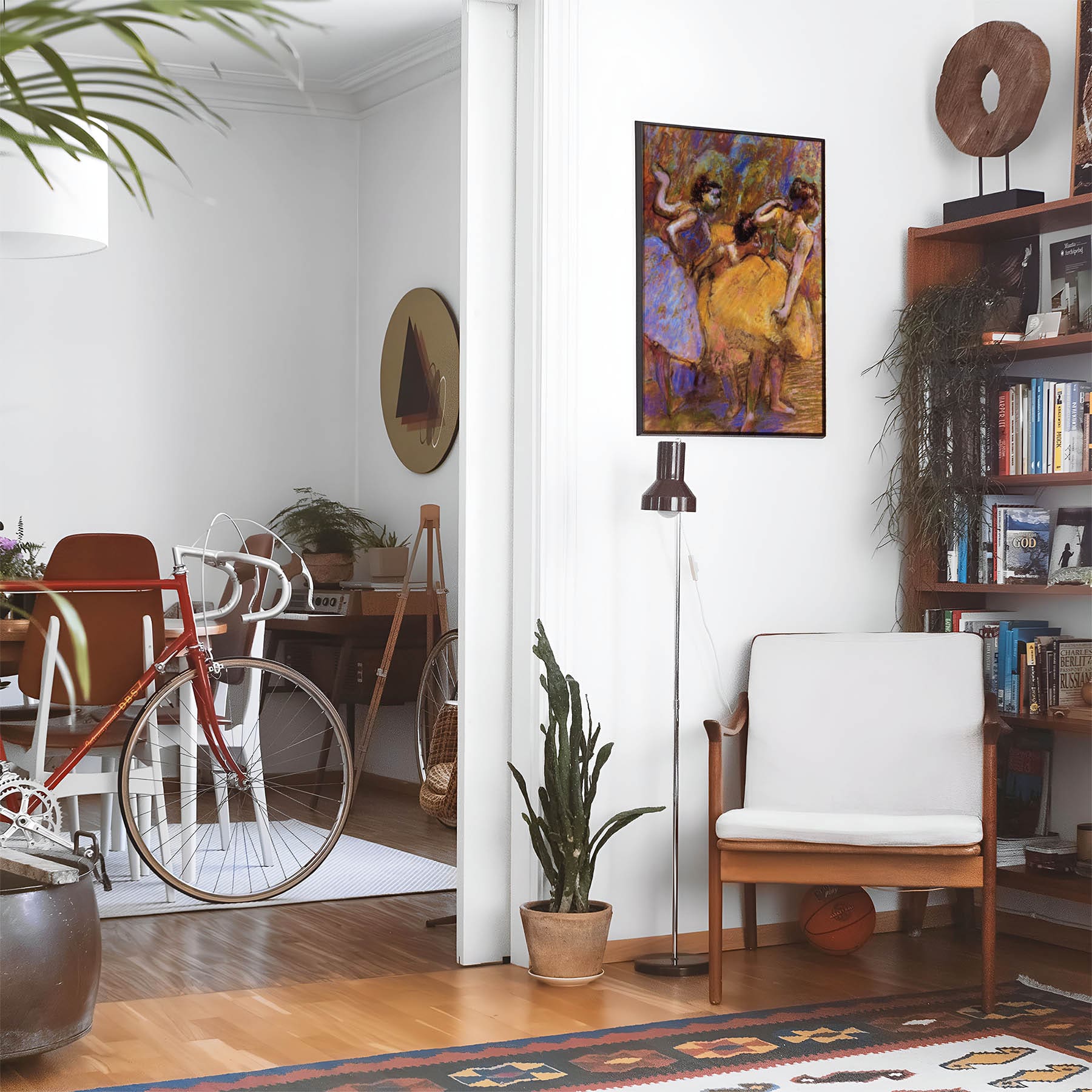Eclectic living room with a road bike, bookshelf and house plants that features framed artwork of a Dancers in Yellow and Violet above a chair and lamp