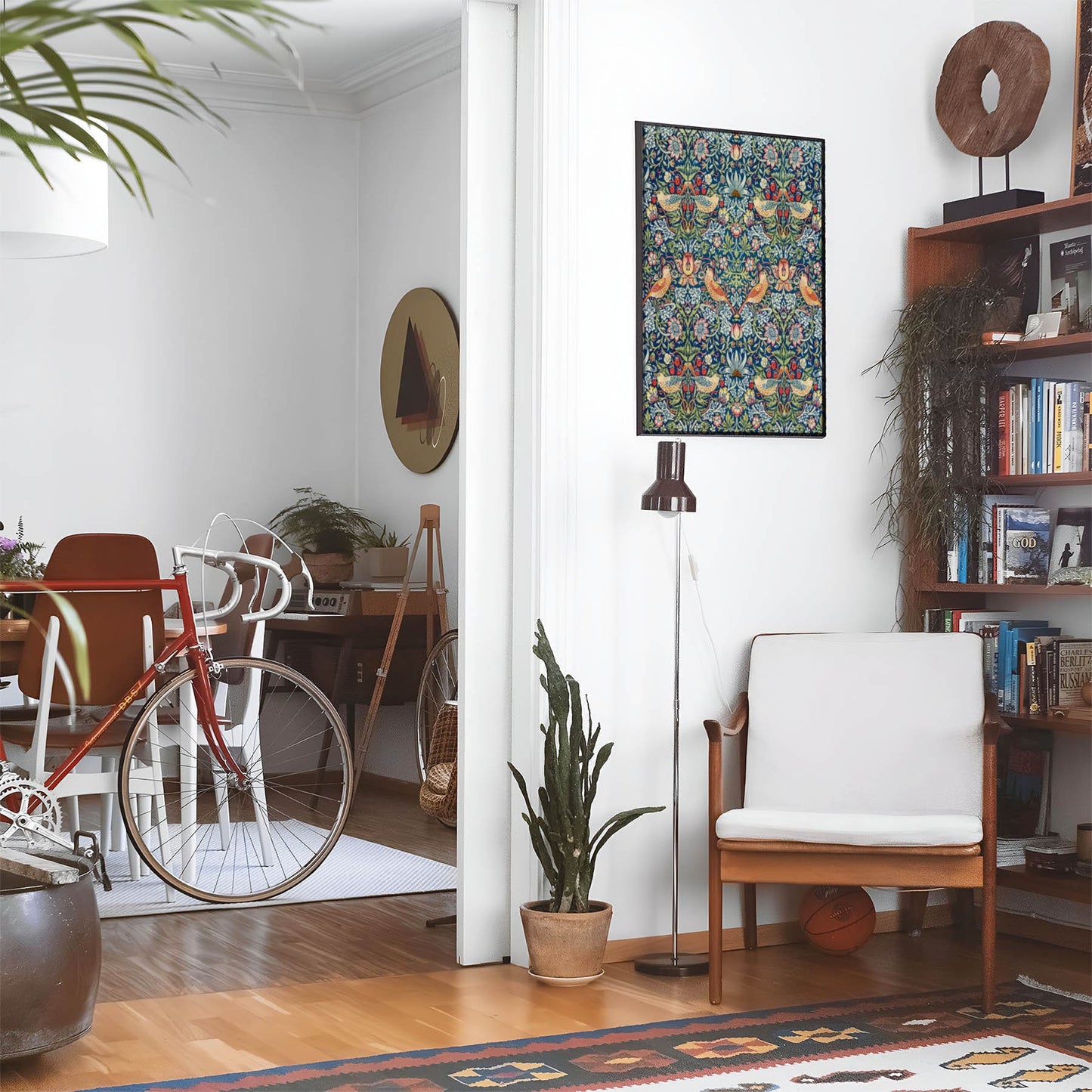 Eclectic living room with a road bike, bookshelf and house plants that features framed artwork of a Colorful Birds and Garden above a chair and lamp