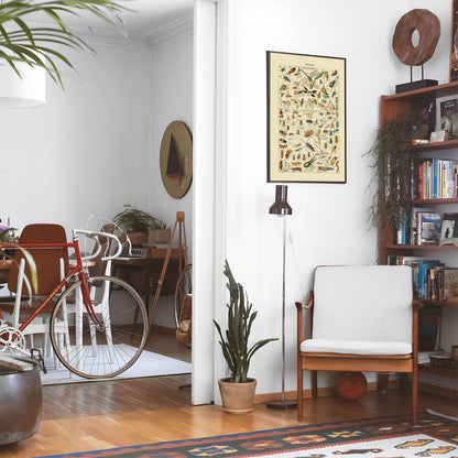 Eclectic living room with a road bike, bookshelf and house plants that features framed artwork of a Insect Identification above a chair and lamp
