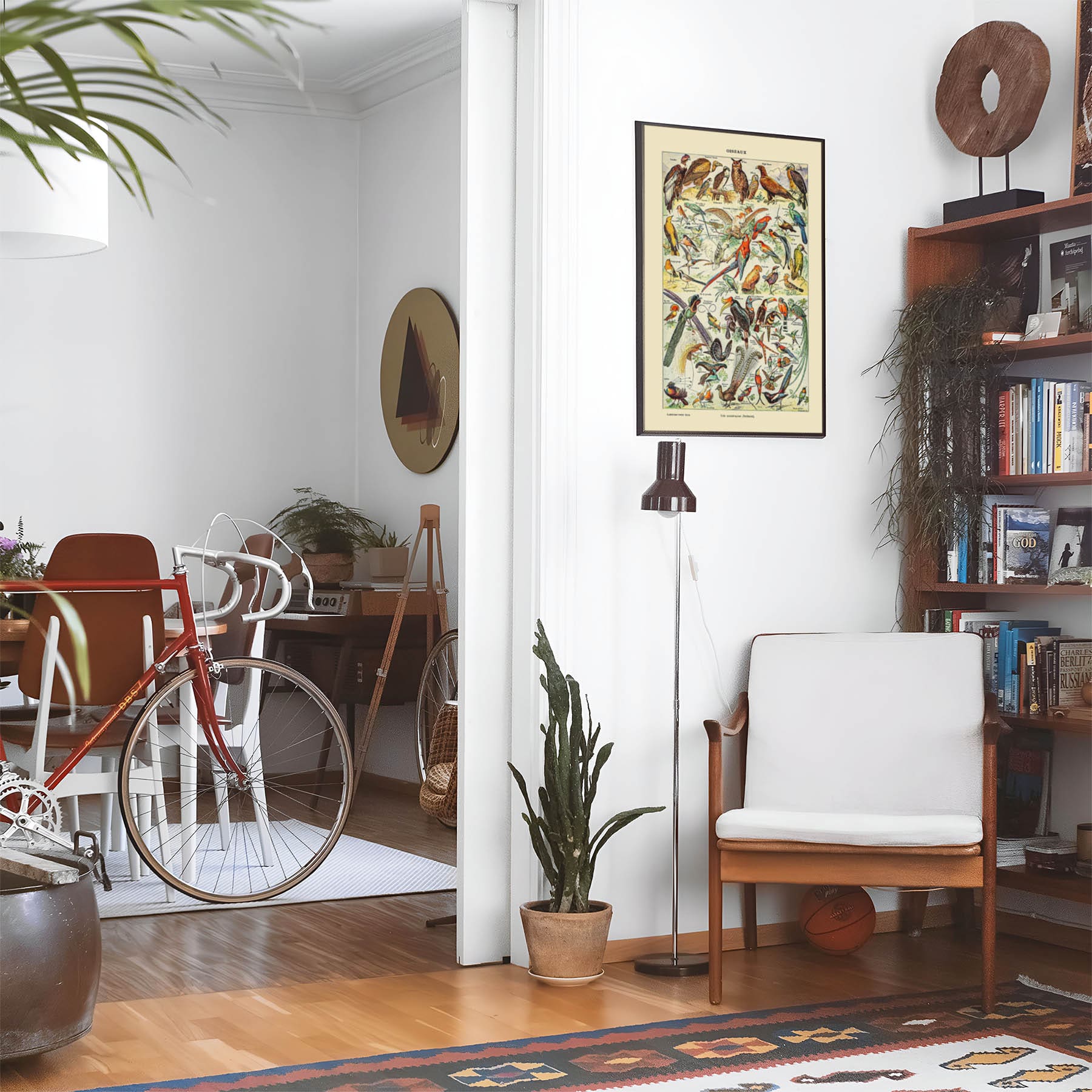 Eclectic living room with a road bike, bookshelf and house plants that features framed artwork of a Wild Birds above a chair and lamp