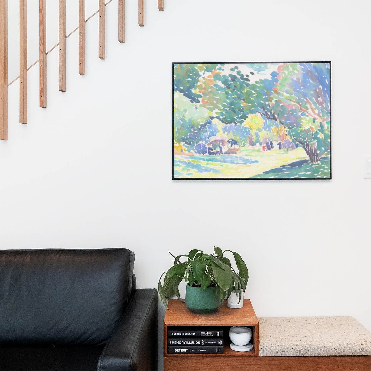 Living space with a black leather couch and table with a plant and books below a staircase featuring a framed picture of Relaxing Watercolor