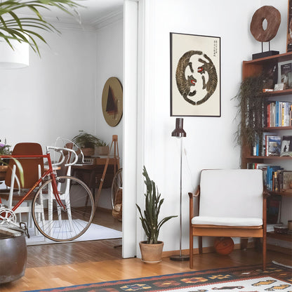 Eclectic living room with a road bike, bookshelf and house plants that features framed artwork of a Two Tigers in a Circle above a chair and lamp