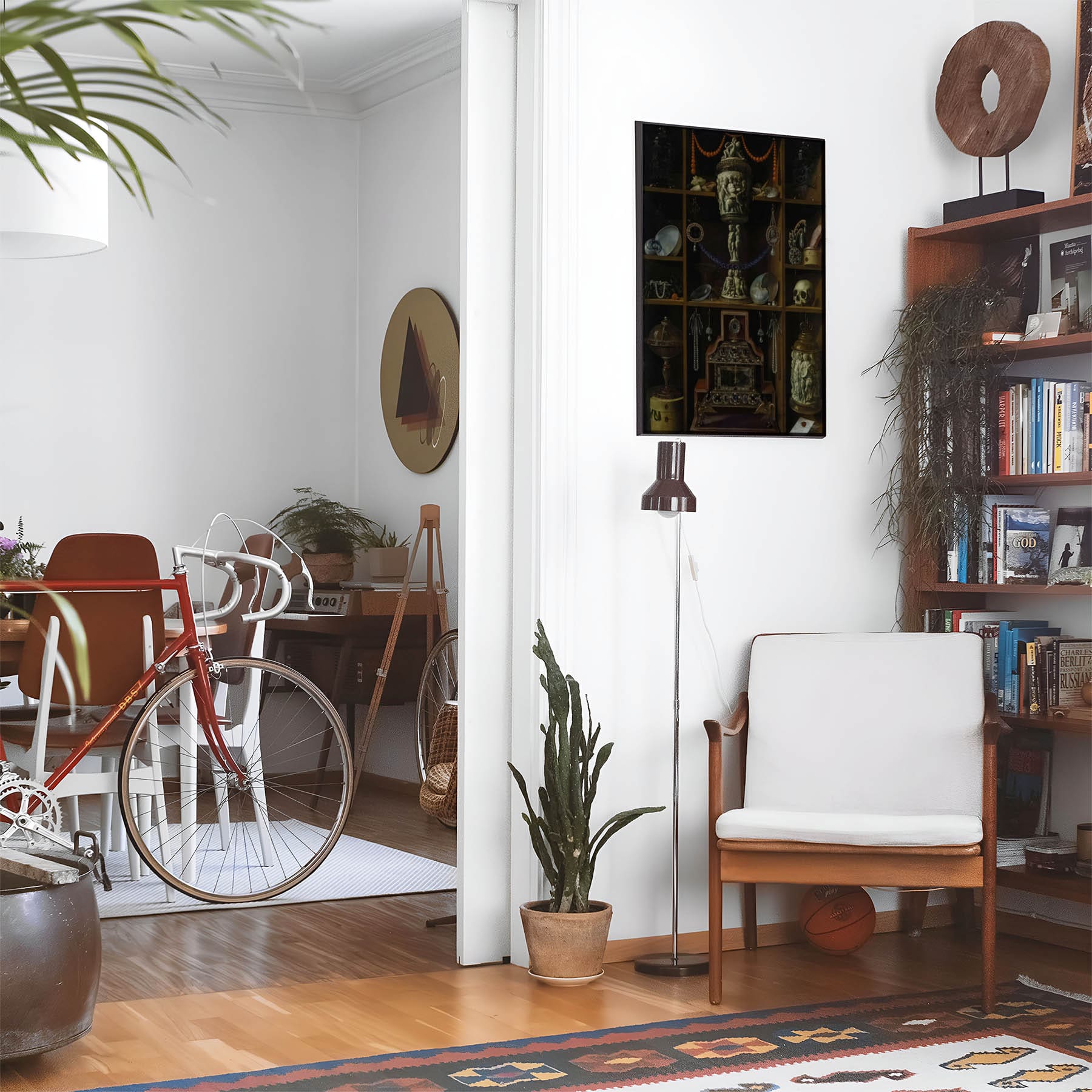 Eclectic living room with a road bike, bookshelf and house plants that features framed artwork of a Vintage Treasure Chest above a chair and lamp