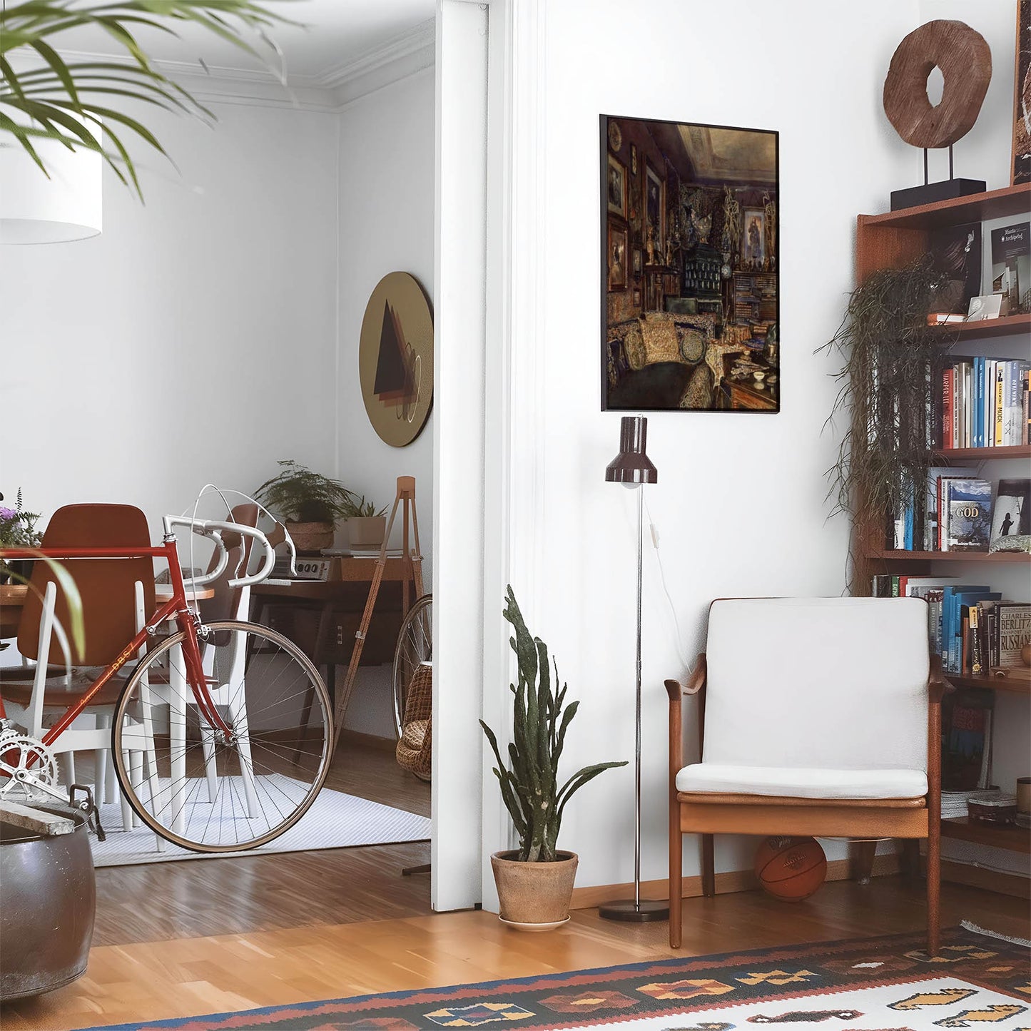 Eclectic living room with a road bike, bookshelf and house plants that features framed artwork of a Gold and Black Couch above a chair and lamp