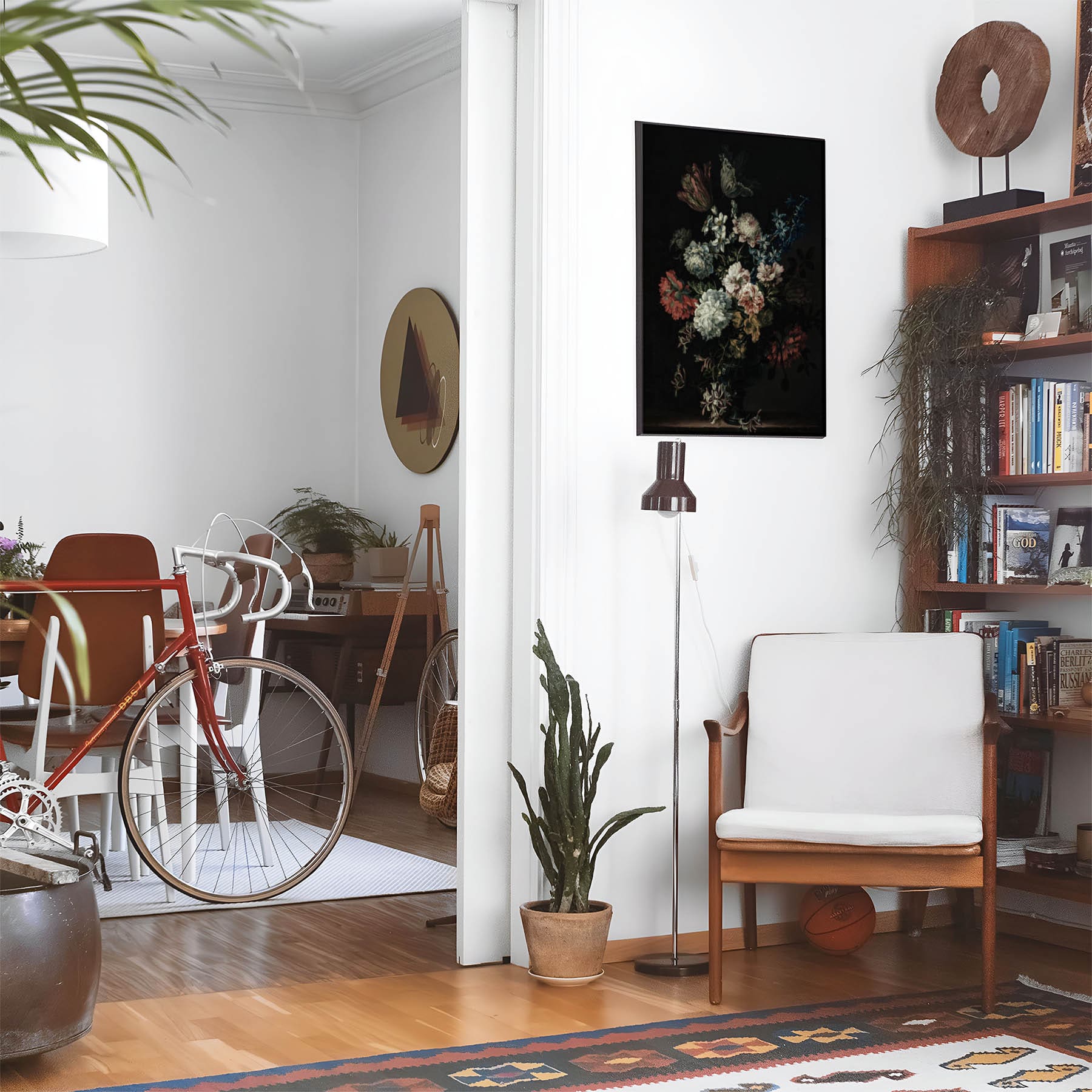 Eclectic living room with a road bike, bookshelf and house plants that features framed artwork of a Dark Still Life Flower above a chair and lamp