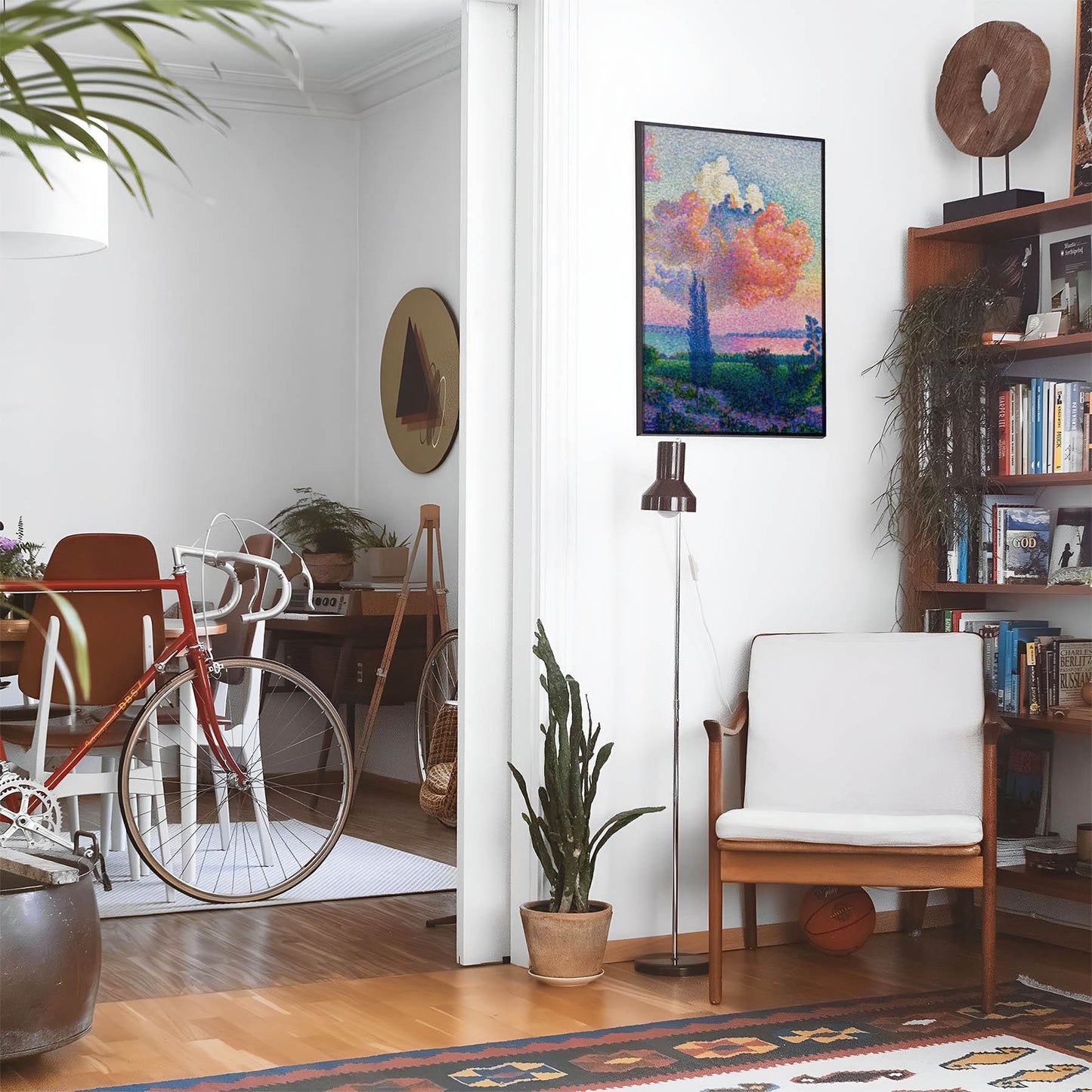 Eclectic living room with a road bike, bookshelf and house plants that features framed artwork of a Beautiful Light Pink Sunset above a chair and lamp