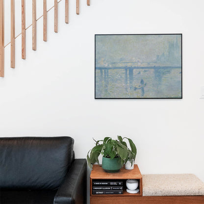 Living space with a black leather couch and table with a plant and books below a staircase featuring a framed picture of Relaxing and Peaceful