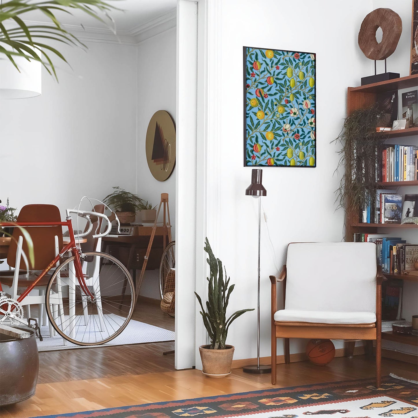 Eclectic living room with a road bike, bookshelf and house plants that features framed artwork of a Lemons above a chair and lamp