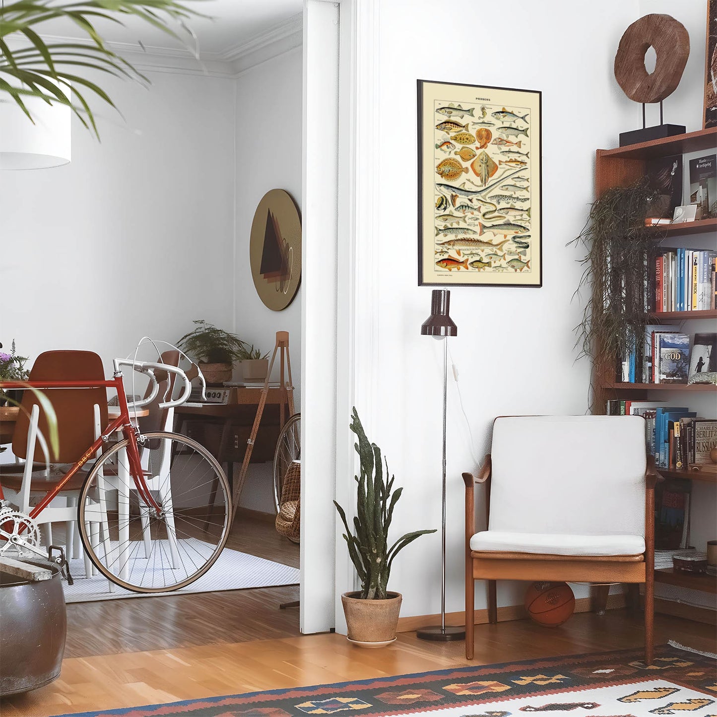 Eclectic living room with a road bike, bookshelf and house plants that features framed artwork of a Diagram of Fish above a chair and lamp