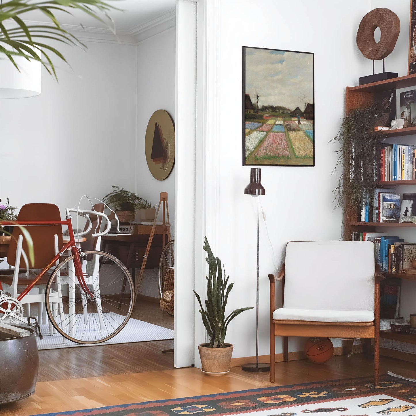 Eclectic living room with a road bike, bookshelf and house plants that features framed artwork of a Antique Field of Flowers above a chair and lamp