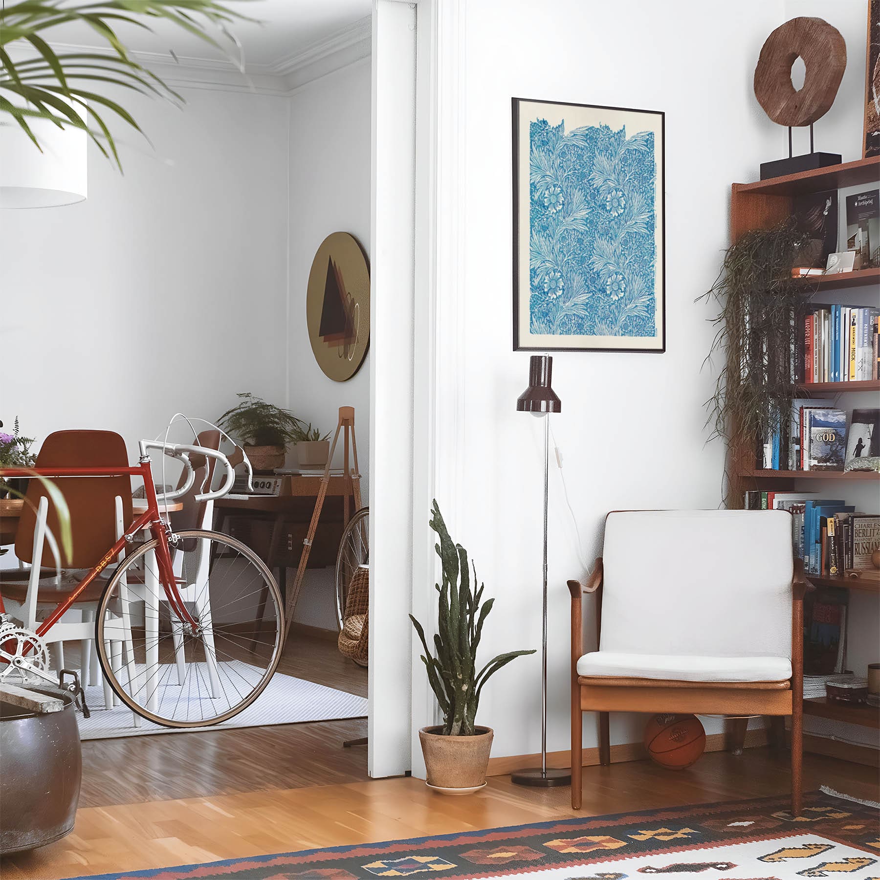 Eclectic living room with a road bike, bookshelf and house plants that features framed artwork of a Boho Flower above a chair and lamp
