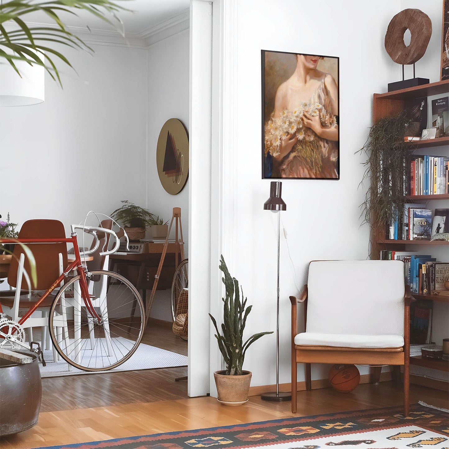 Eclectic living room with a road bike, bookshelf and house plants that features framed artwork of a Woman Holding Daisies above a chair and lamp