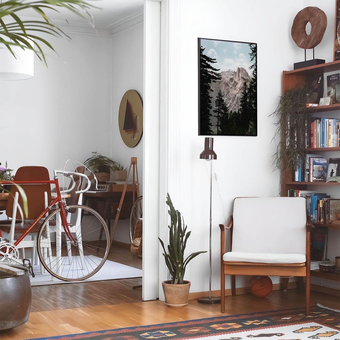 Eclectic living room with a road bike, bookshelf and house plants that features framed artwork of a Vintage Yosemite Valley National Park above a chair and lamp