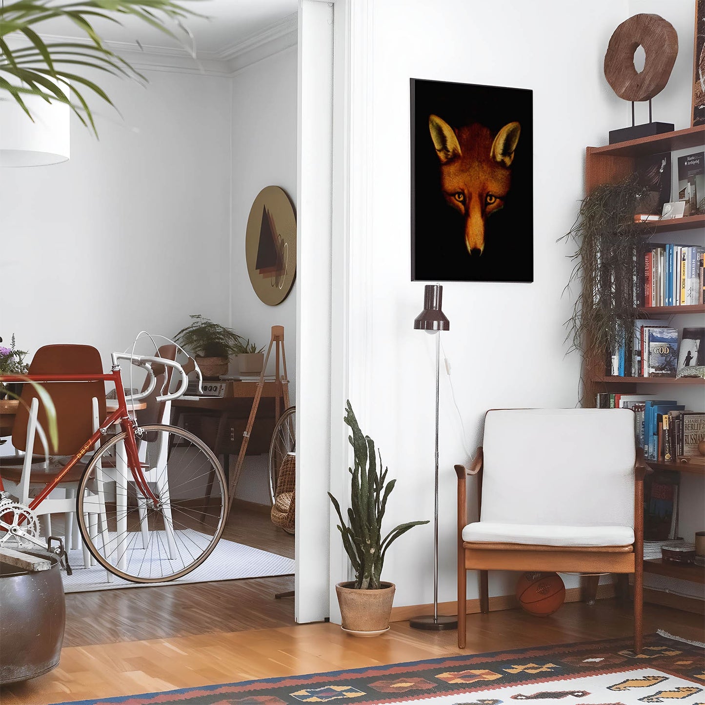 Eclectic living room with a road bike, bookshelf and house plants that features framed artwork of a Large Red Fox Head above a chair and lamp