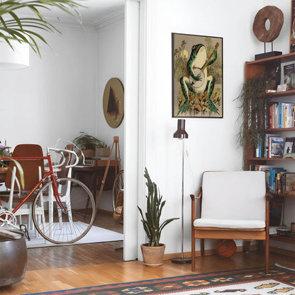 Eclectic living room with a road bike, bookshelf and house plants that features framed artwork of a Cute Frog above a chair and lamp