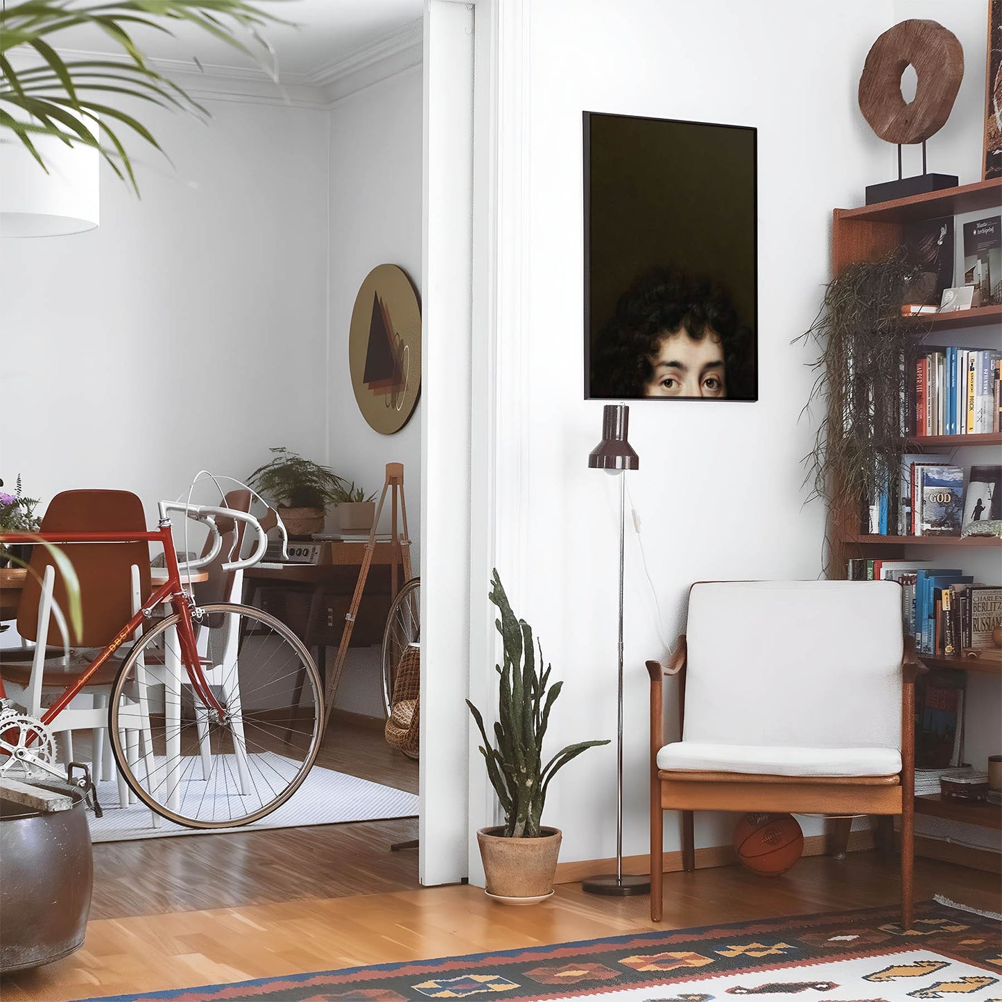 Eclectic living room with a road bike, bookshelf and house plants that features framed artwork of a Funny Vintage above a chair and lamp