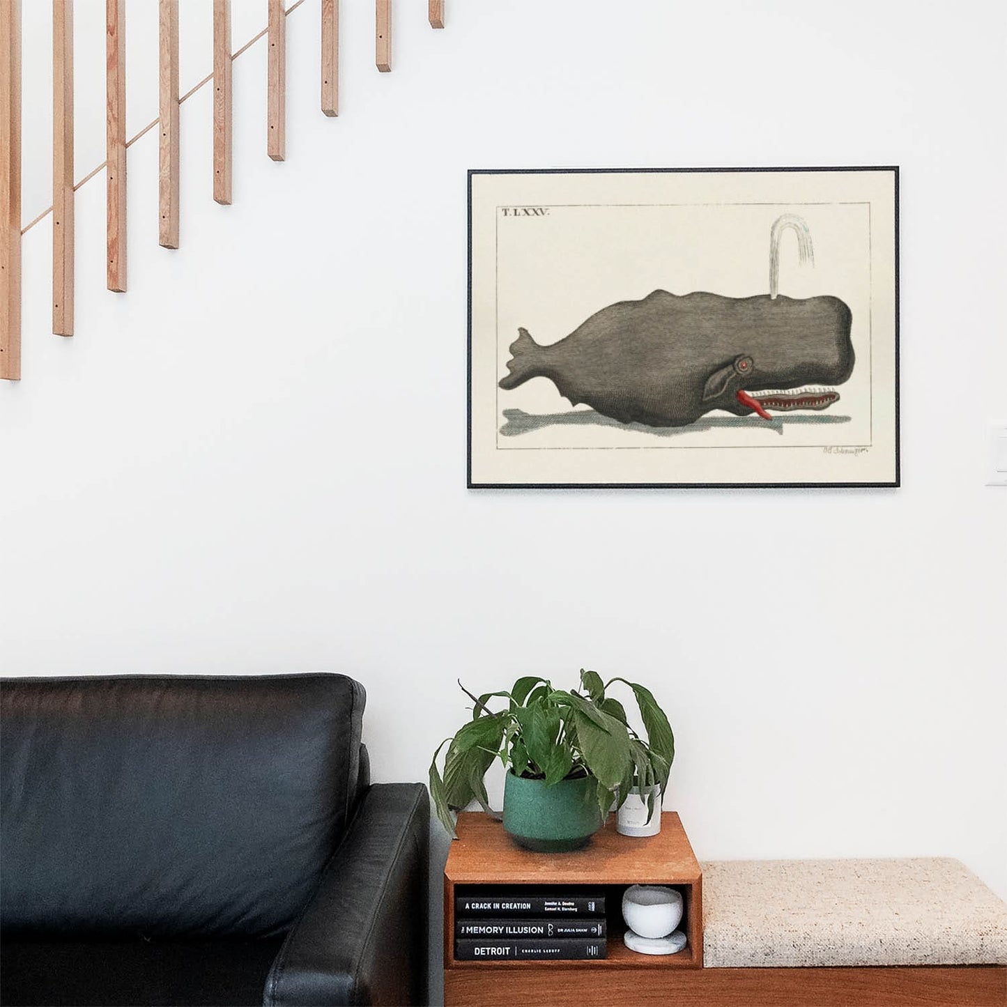 Living space with a black leather couch and table with a plant and books below a staircase featuring a framed picture of Large Gray Whale