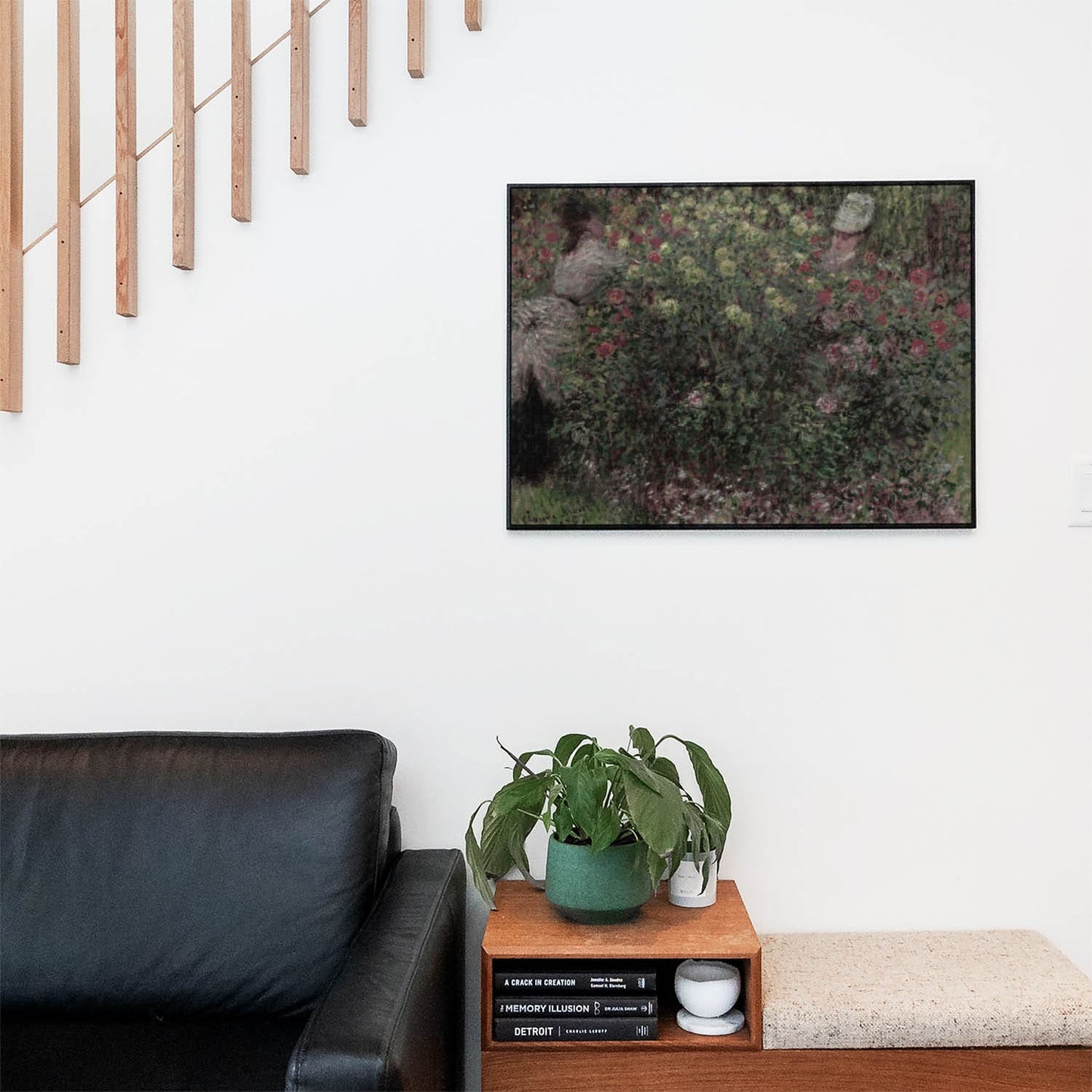 Living space with a black leather couch and table with a plant and books below a staircase featuring a framed picture of Dark Green and Floral