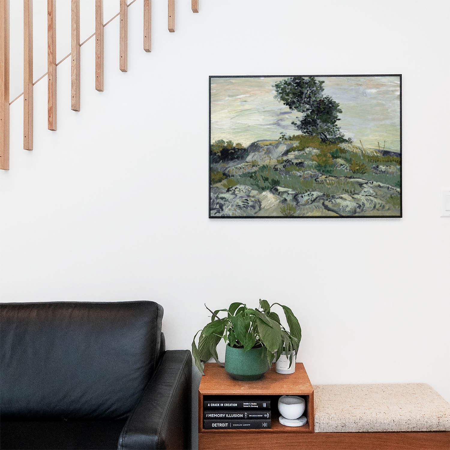 Living space with a black leather couch and table with a plant and books below a staircase featuring a framed picture of Brushstrokes of Nature