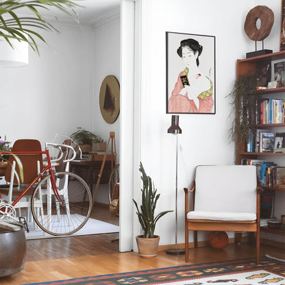 Eclectic living room with a road bike, bookshelf and house plants that features framed artwork of a Green and Red Kimono above a chair and lamp