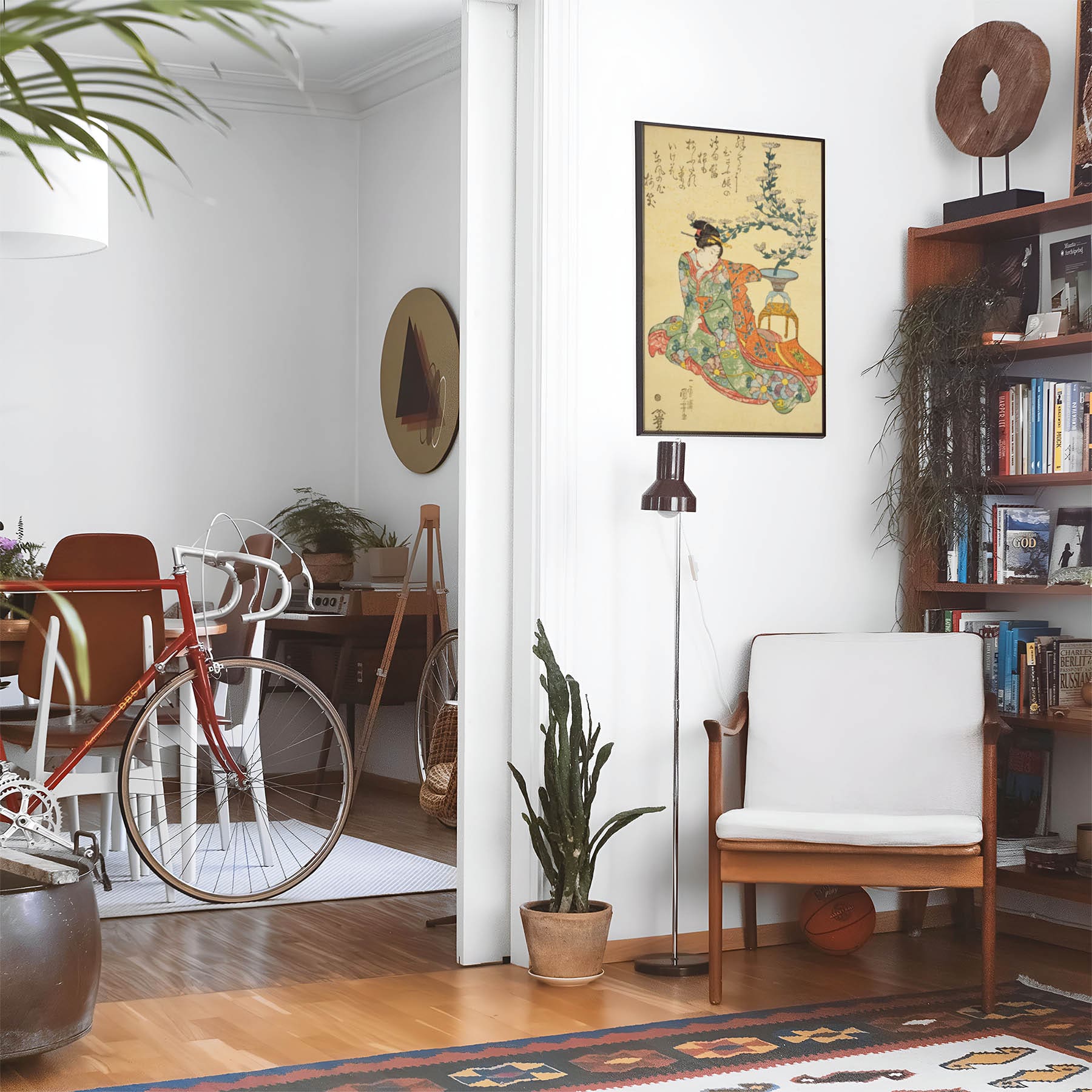 Eclectic living room with a road bike, bookshelf and house plants that features framed artwork of a Light Green and Yellow Woodblock above a chair and lamp