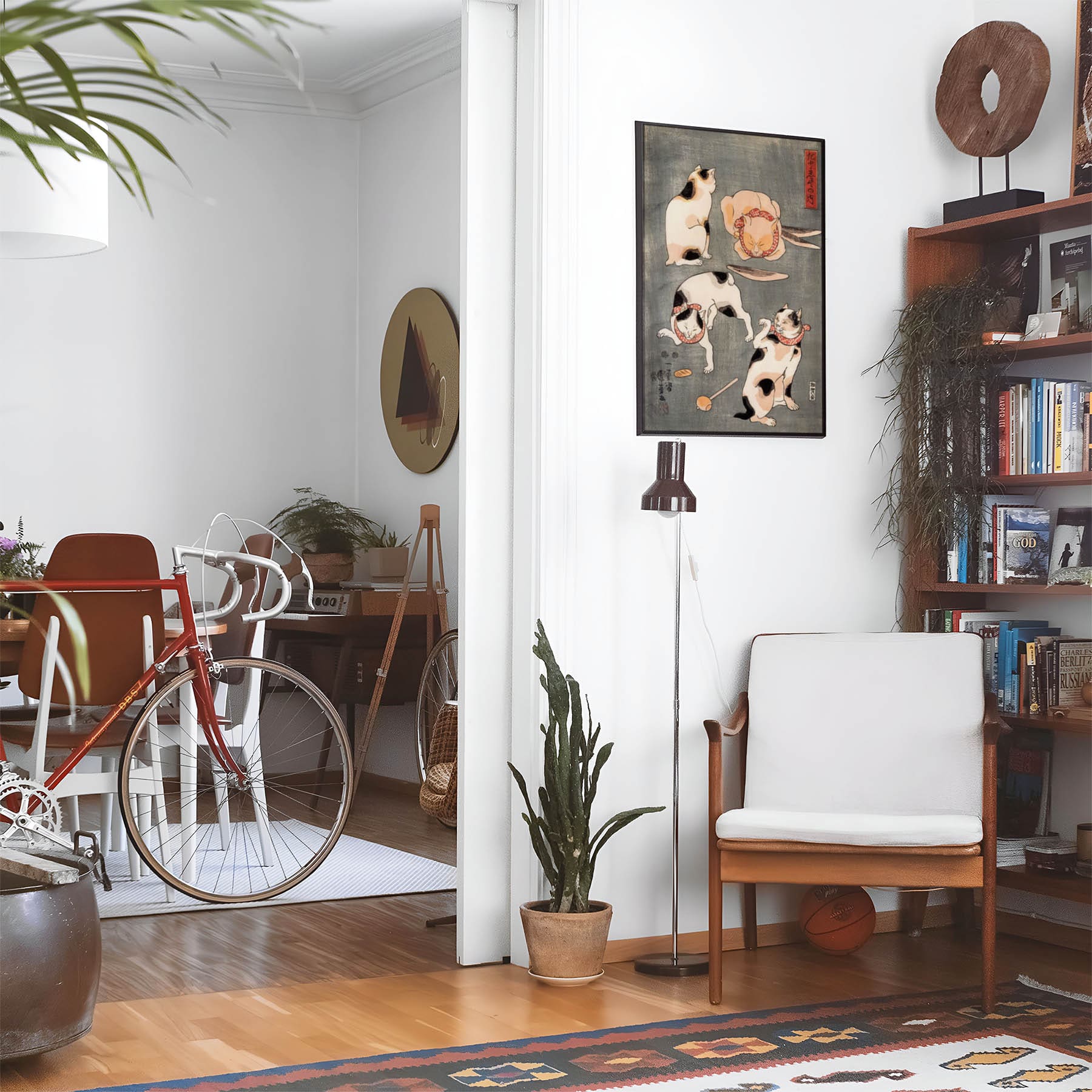 Eclectic living room with a road bike, bookshelf and house plants that features framed artwork of a Cats Playing above a chair and lamp