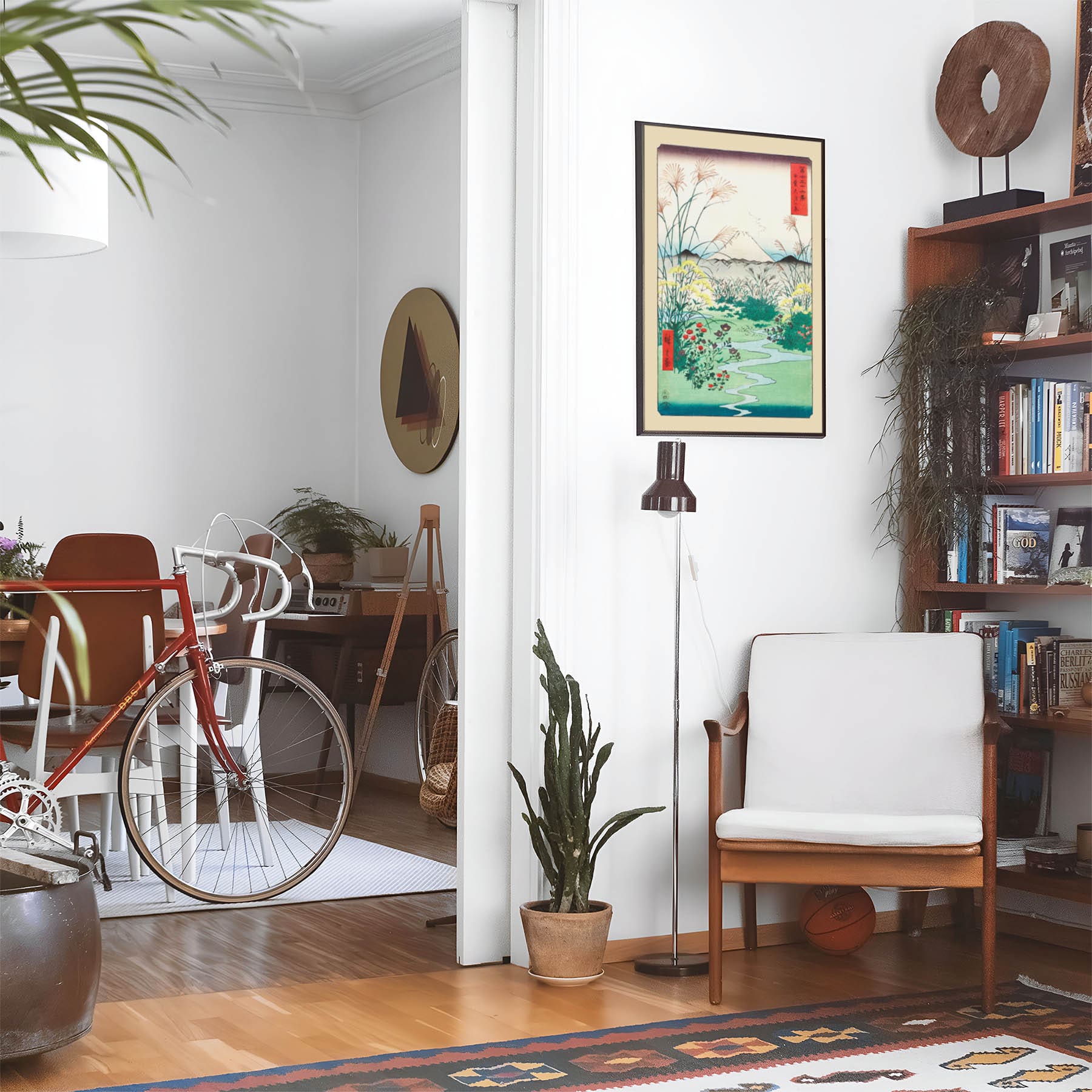 Eclectic living room with a road bike, bookshelf and house plants that features framed artwork of a River and Mountain Woodblock above a chair and lamp