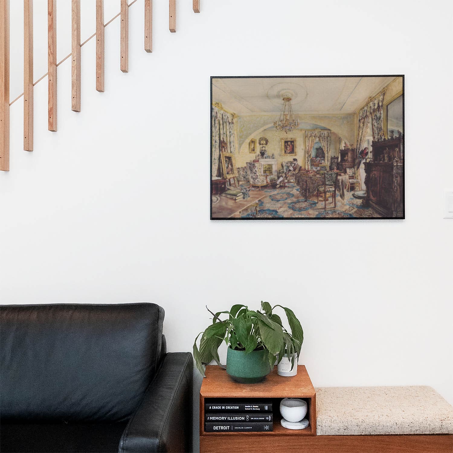 Living space with a black leather couch and table with a plant and books below a staircase featuring a framed picture of The Living Room