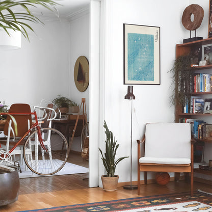 Eclectic living room with a road bike, bookshelf and house plants that features framed artwork of a Aesthetic Japanese above a chair and lamp