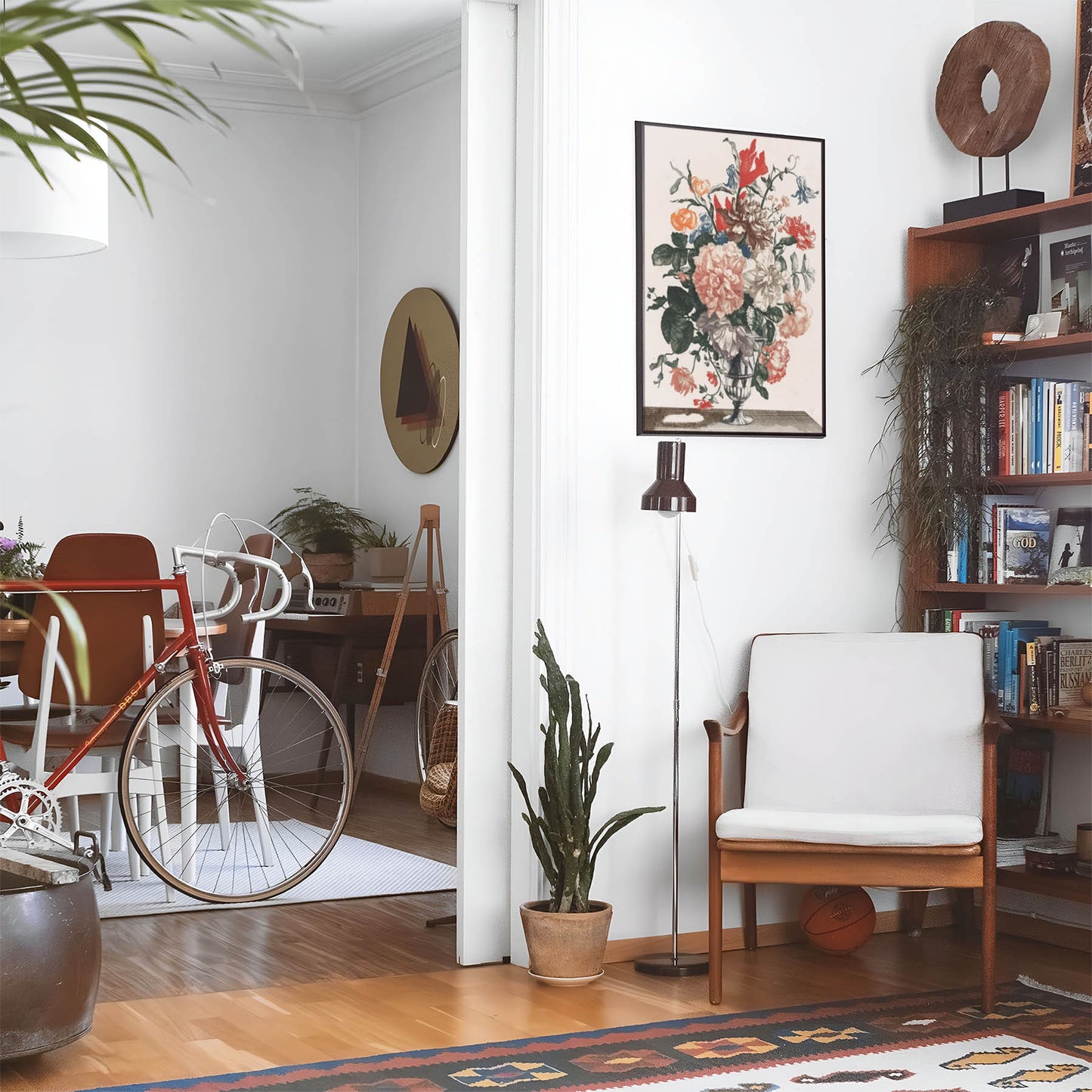 Eclectic living room with a road bike, bookshelf and house plants that features framed artwork of a Flower Bouquet above a chair and lamp