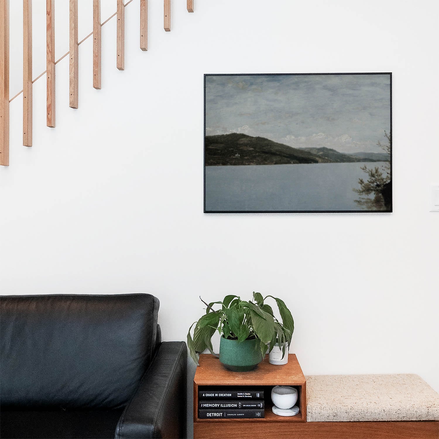 Living space with a black leather couch and table with a plant and books below a staircase featuring a framed picture of Blue and Green Nature