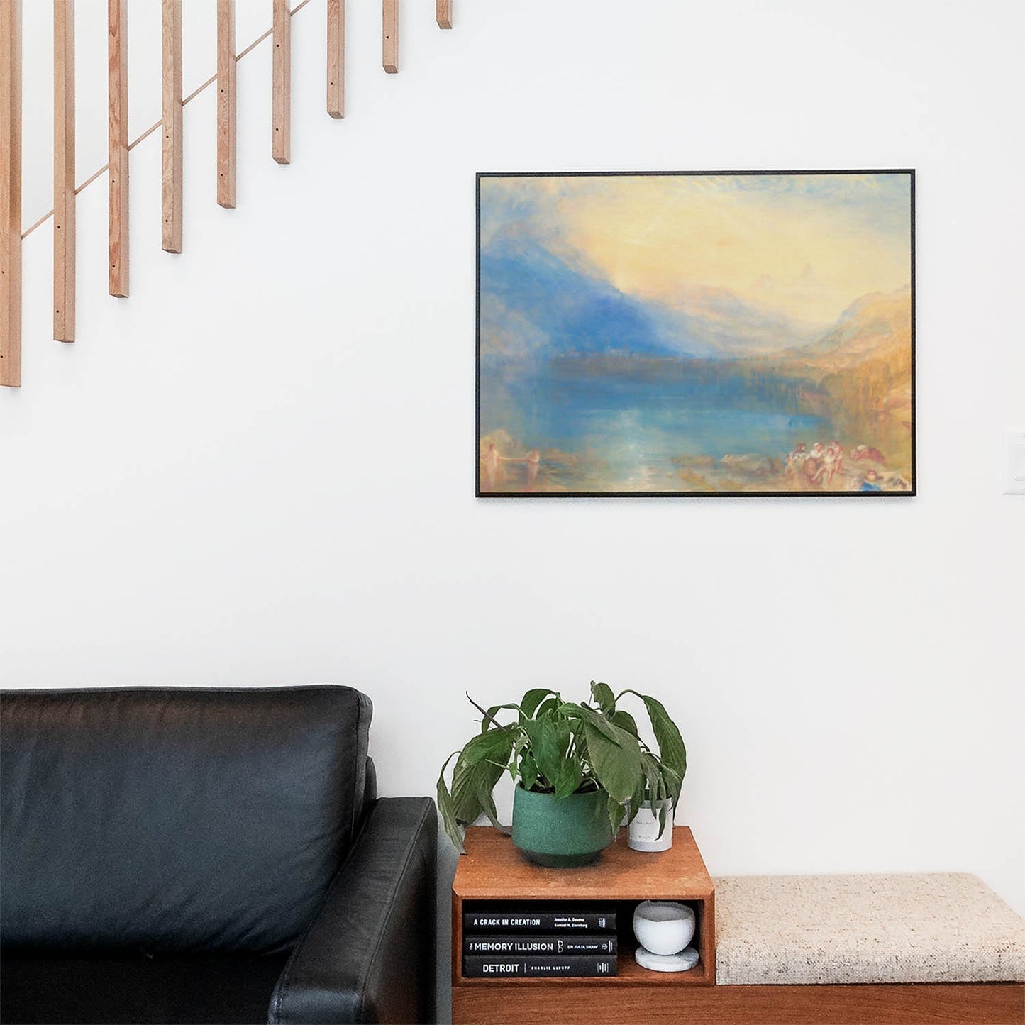 Living space with a black leather couch and table with a plant and books below a staircase featuring a framed picture of Yellow and Blue