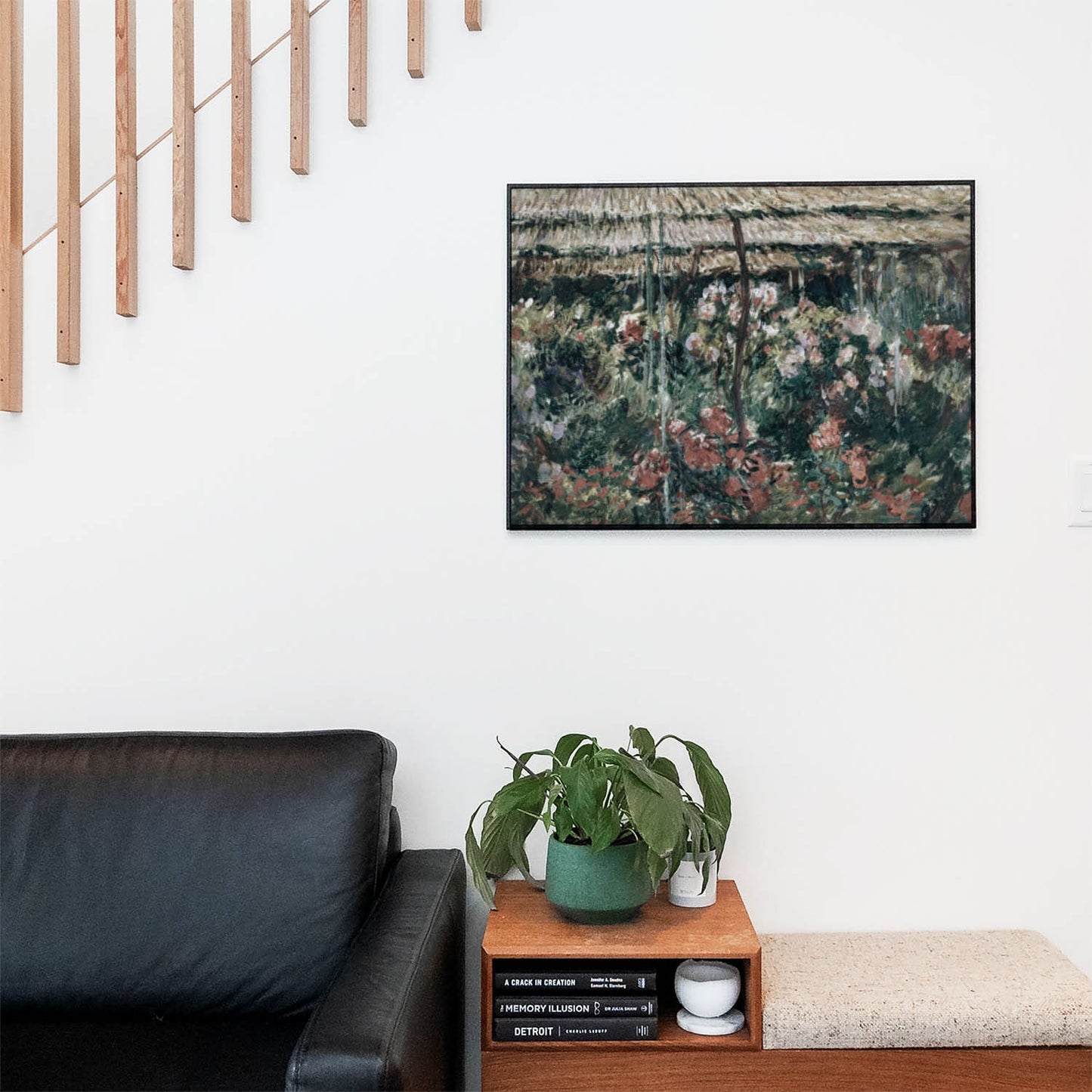 Living space with a black leather couch and table with a plant and books below a staircase featuring a framed picture of Relaxing Floral