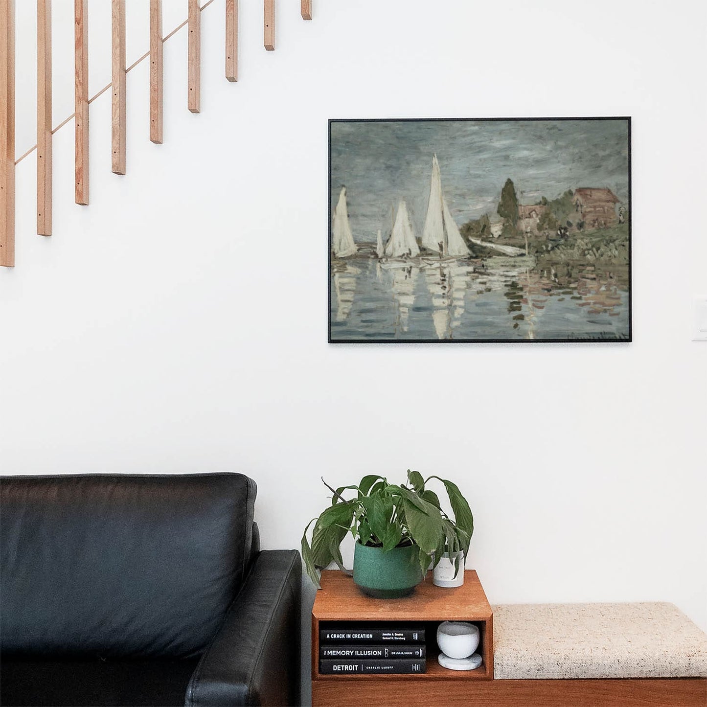 Living space with a black leather couch and table with a plant and books below a staircase featuring a framed picture of Sail Boats