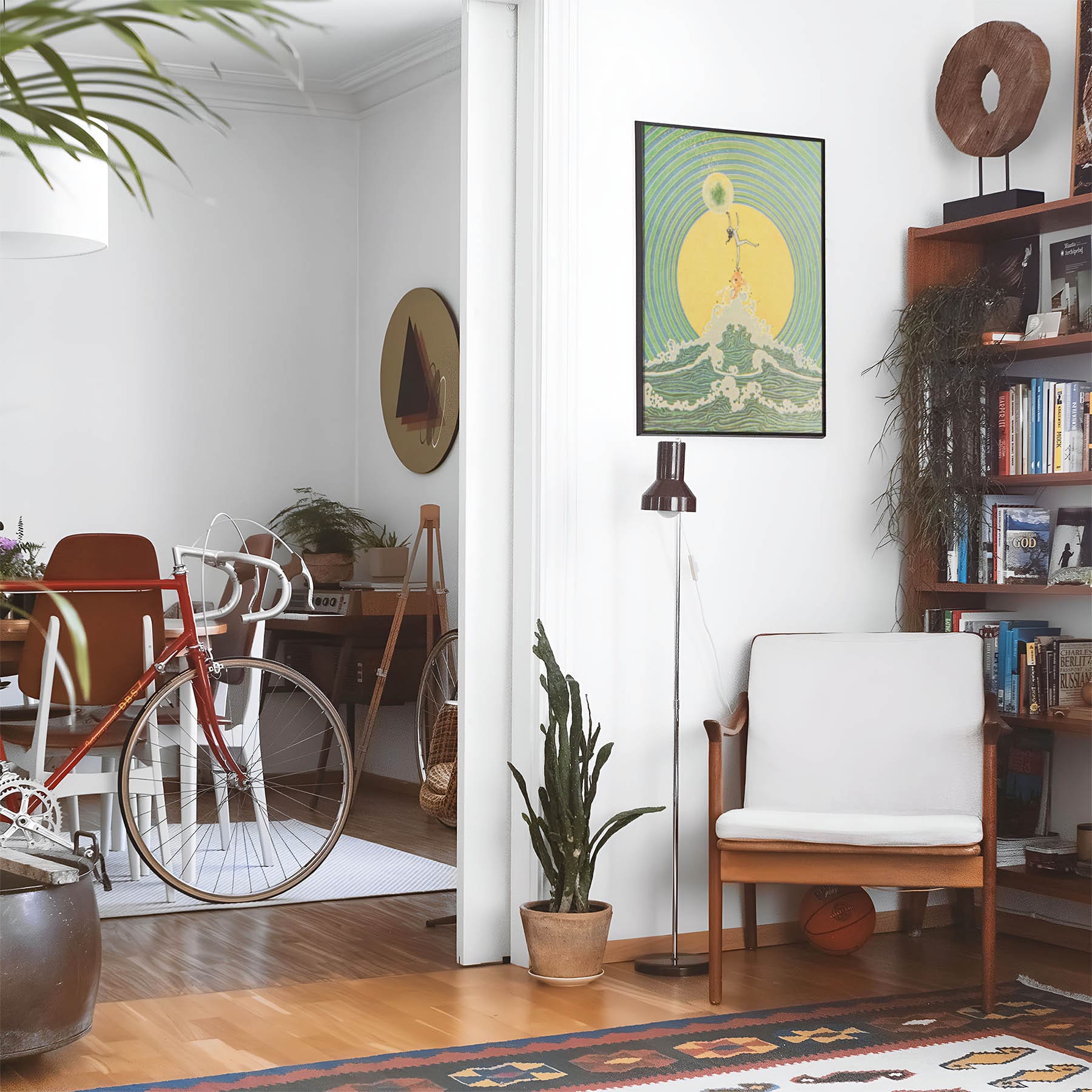Eclectic living room with a road bike, bookshelf and house plants that features framed artwork of a Green and Yellow Fantasy above a chair and lamp