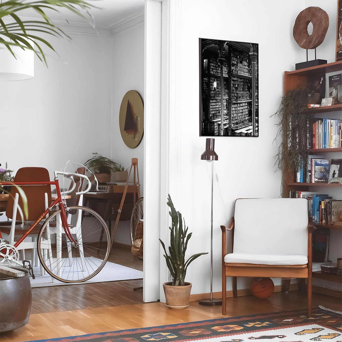 Eclectic living room with a road bike, bookshelf and house plants that features framed artwork of a Black and White Library above a chair and lamp