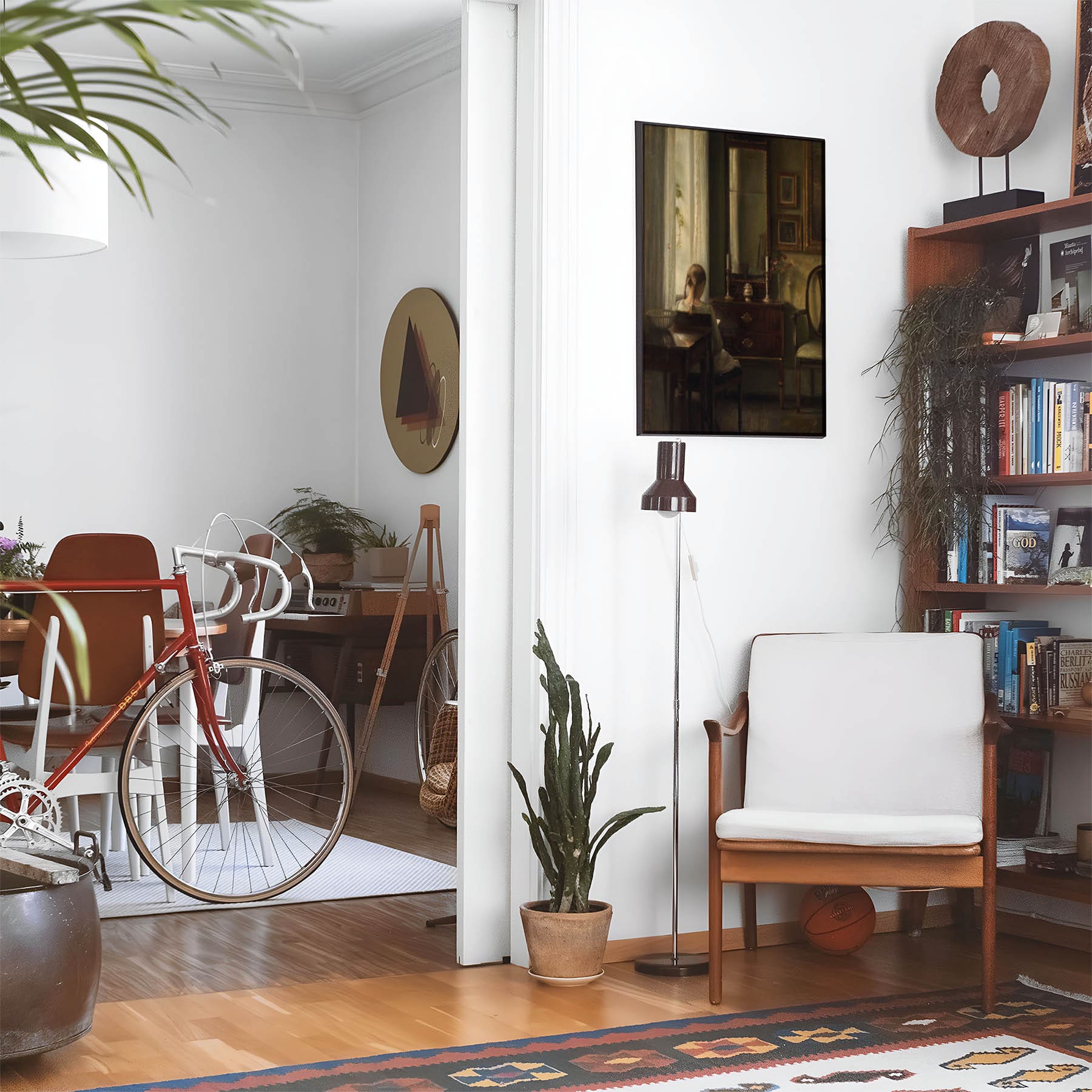 Eclectic living room with a road bike, bookshelf and house plants that features framed artwork of a A Quiet Read above a chair and lamp