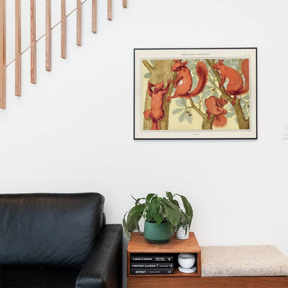 Living space with a black leather couch and table with a plant and books below a staircase featuring a framed picture of Four Squirrels in a Tree